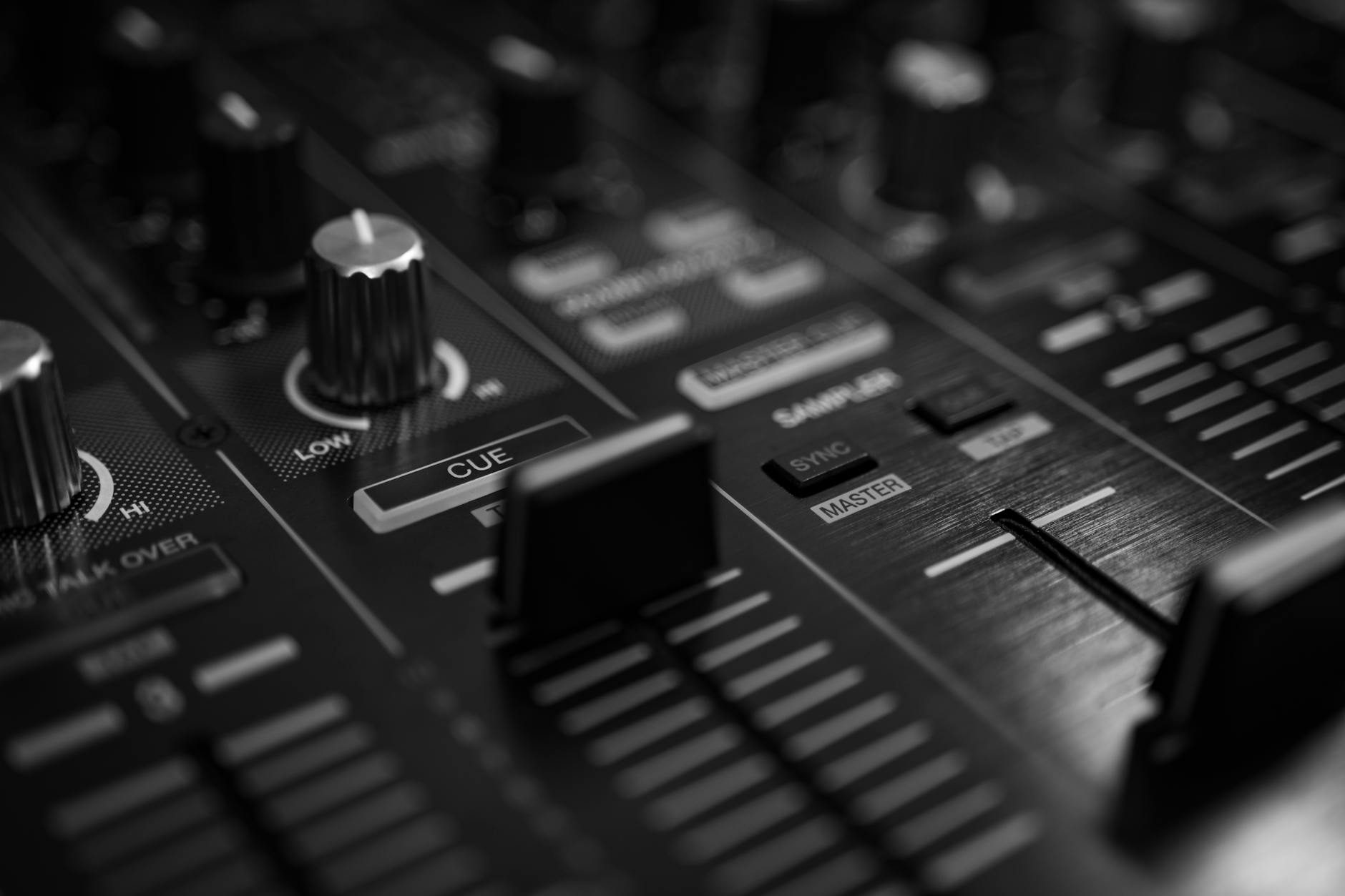 world music w elektronice - High-contrast close-up of an audio mixer with sliders and knobs in a black and white tone.