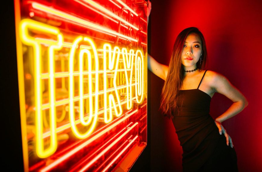 Gen Z oczekuje immersywnych doświadczeń - A stylish woman poses by a vibrant Tokyo neon sign, exuding modern urban nightlife.