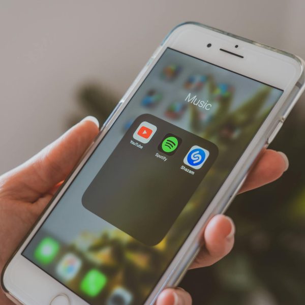 spotify discovery mode payola - Hand holding a smartphone displaying popular music apps like Spotify and Shazam in a close-up