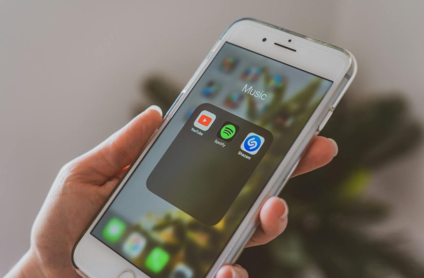 spotify discovery mode payola - Hand holding a smartphone displaying popular music apps like Spotify and Shazam in a close-up