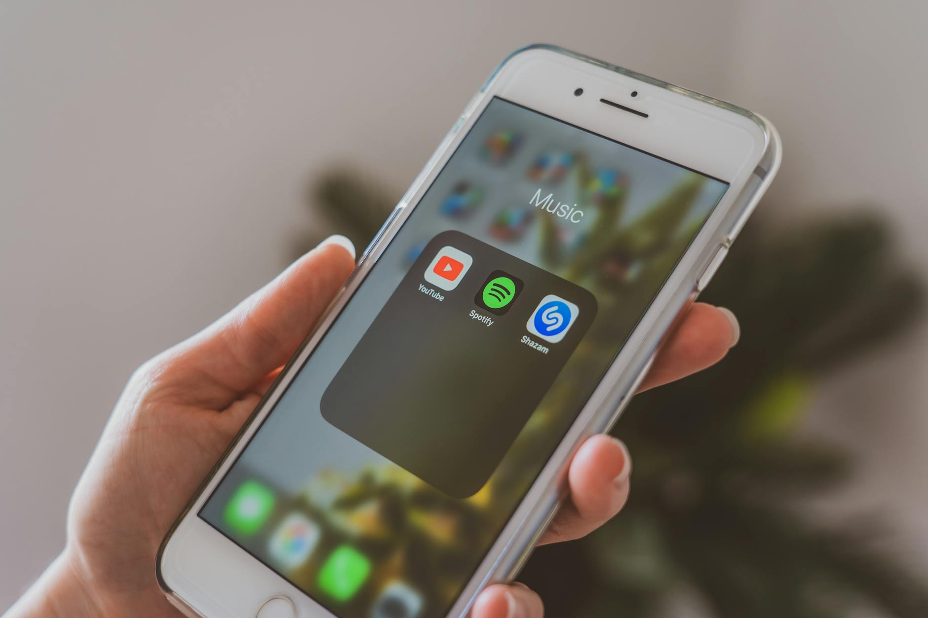 spotify discovery mode payola - Hand holding a smartphone displaying popular music apps like Spotify and Shazam in a close-up