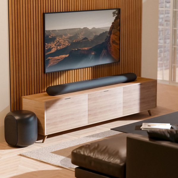 Czarny soundbar Bluesound PULSE CINEMA pod telewizorem i subwoofer PULSE SUB w jasnym salonie