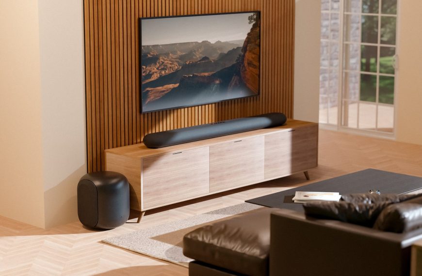 Czarny soundbar Bluesound PULSE CINEMA pod telewizorem i subwoofer PULSE SUB w jasnym salonie