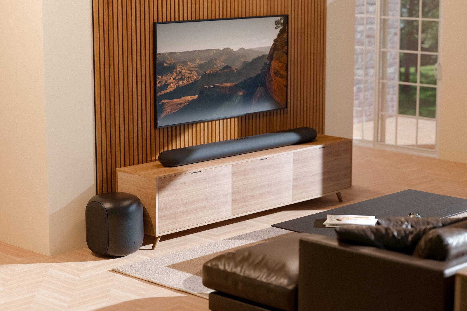 Czarny soundbar Bluesound PULSE CINEMA pod telewizorem i subwoofer PULSE SUB w jasnym salonie