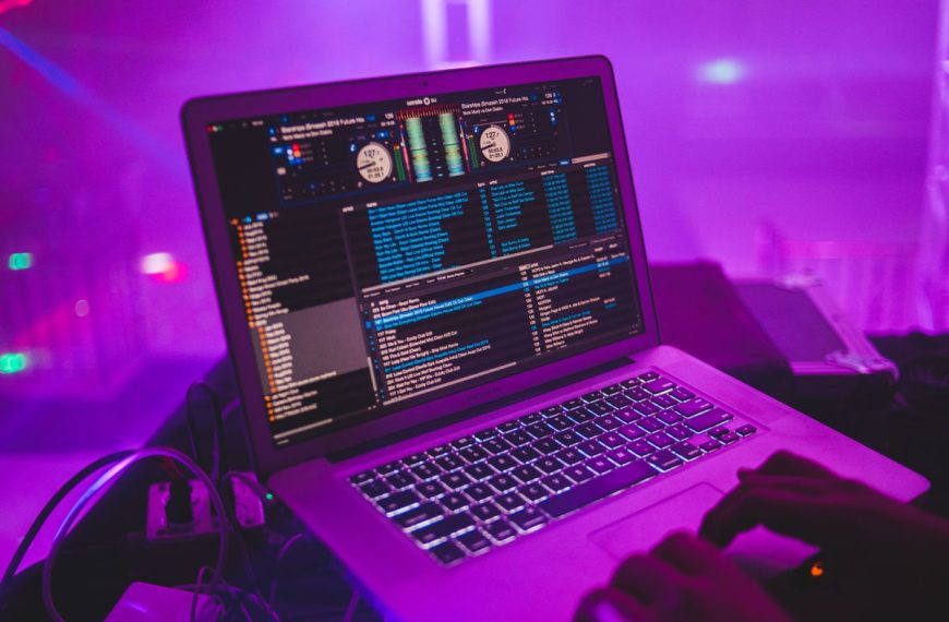 DJ pracuje przy laptopie w klubie o fioletowym oświetleniu, fotografia poglądowa do artykułu o dystrybucji muzyki