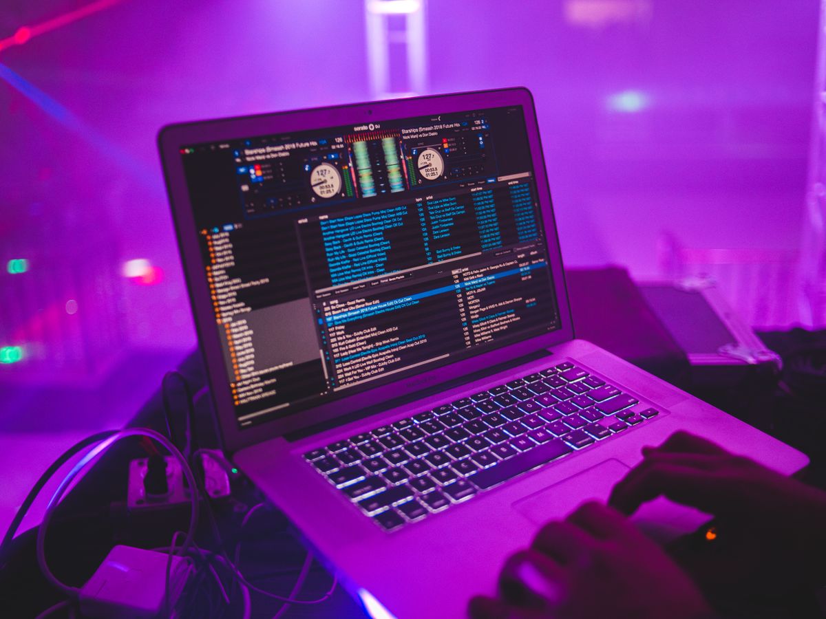 DJ pracuje przy laptopie w klubie o fioletowym oświetleniu, fotografia poglądowa do artykułu o dystrybucji muzyki
